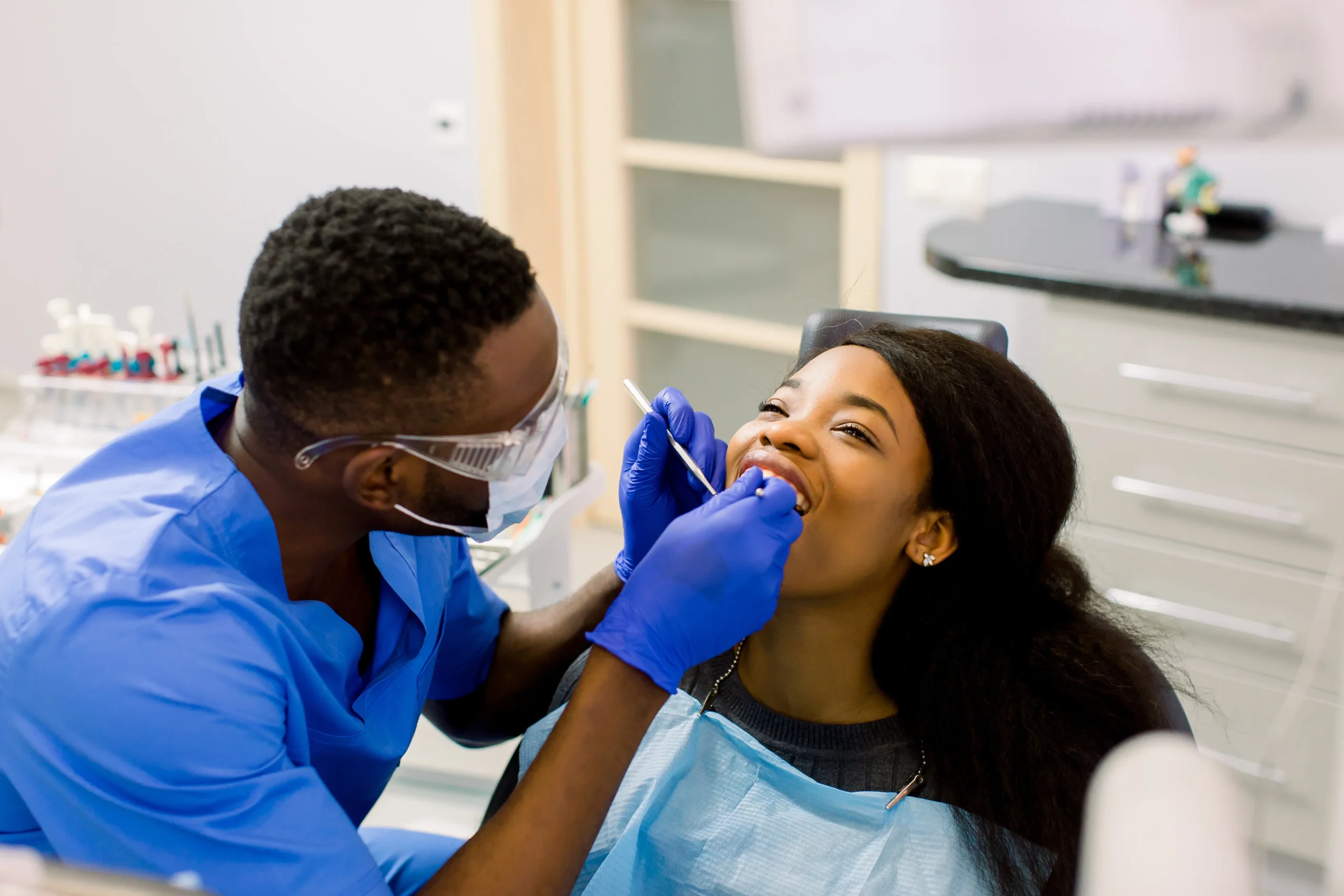Male african dentist examining a patient with tools in dental clinic.