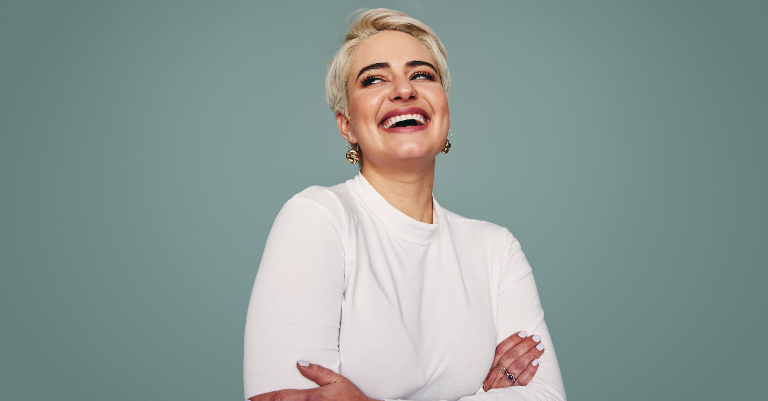 Beautiful blonde woman laughing in a studio. Happy mid-adult woman looking away cheerfully while standing against a studio background. Fashionable woman feeling confident.