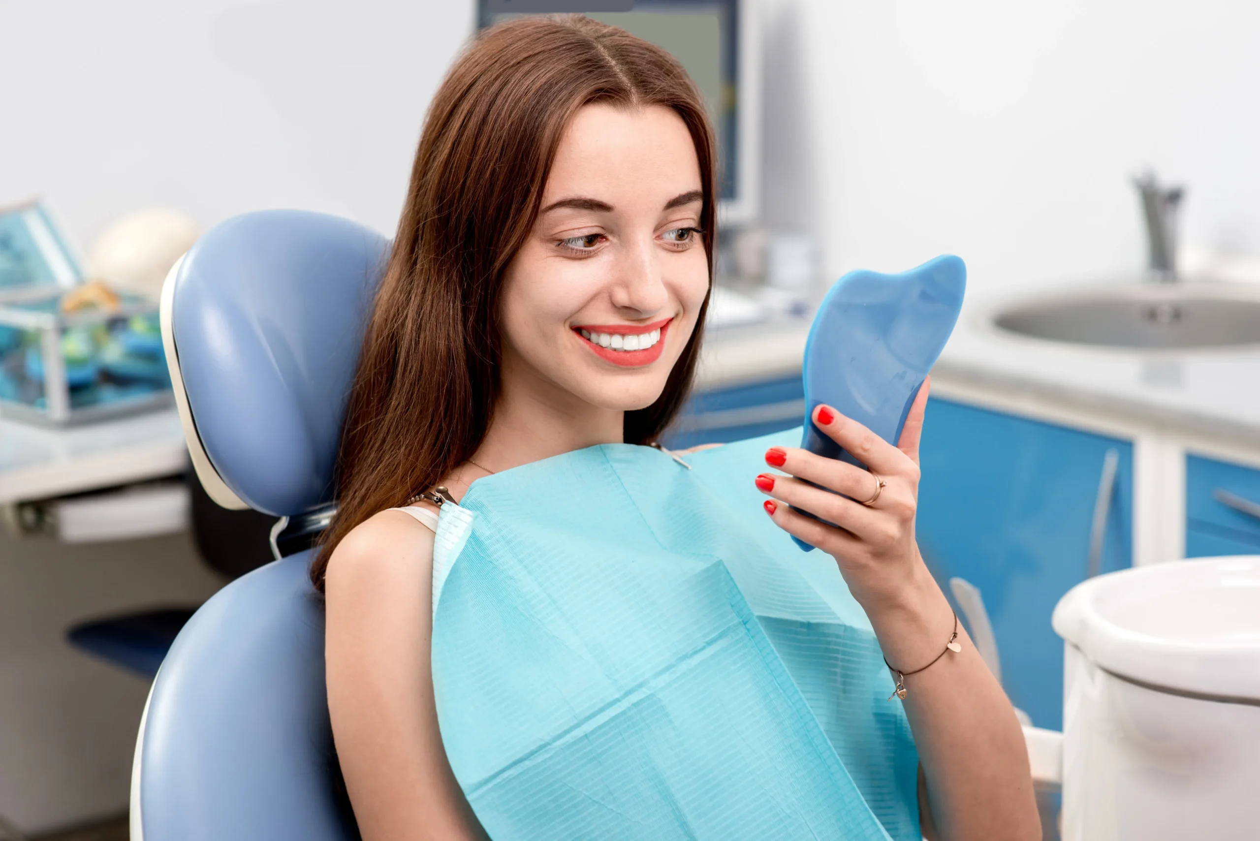 Young woman patient looking at her teeth in the mirror in the dental office